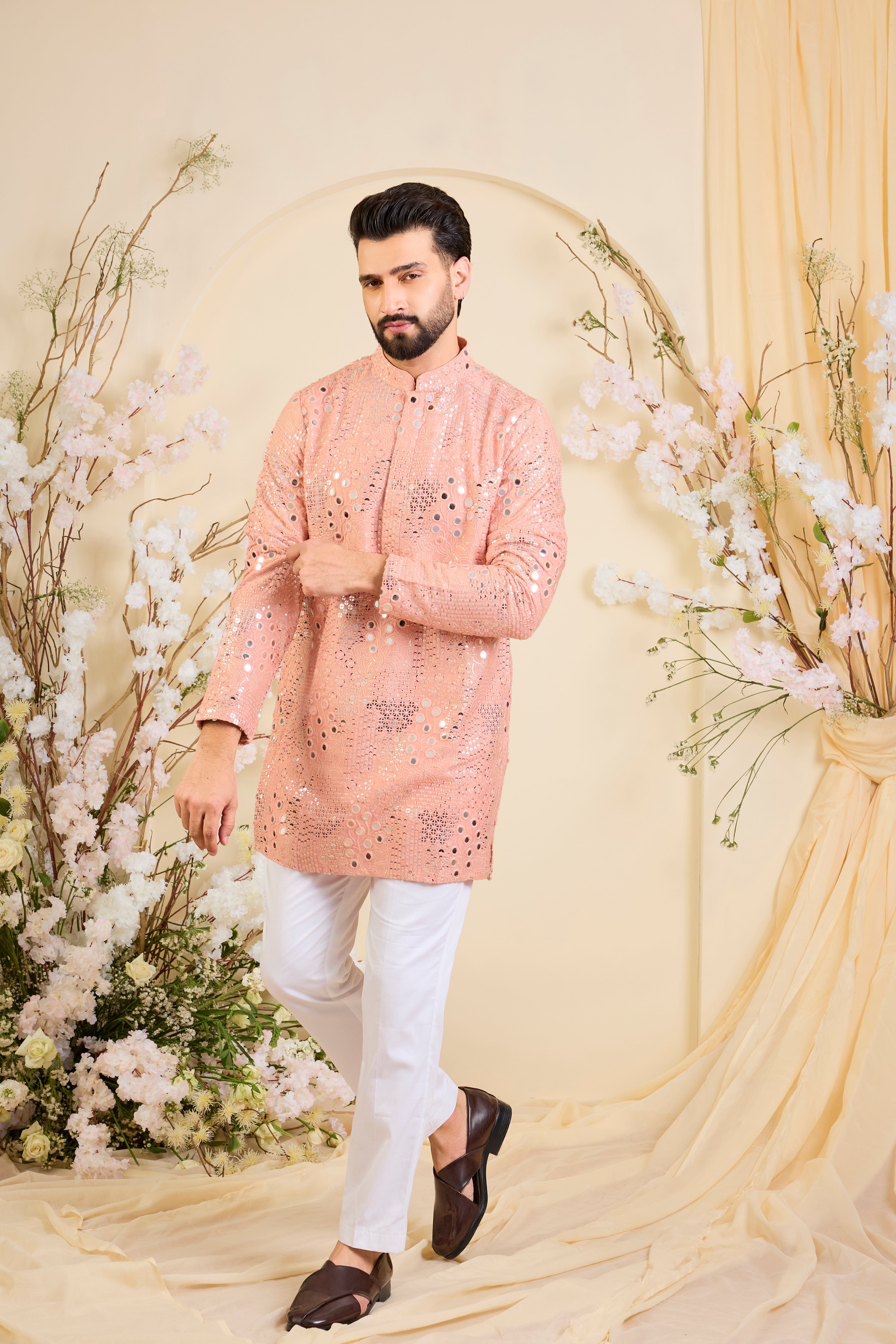 A peach short kurta enriched with intricate mirror work, delicate floral embroidery, and dense sequin detailing.
