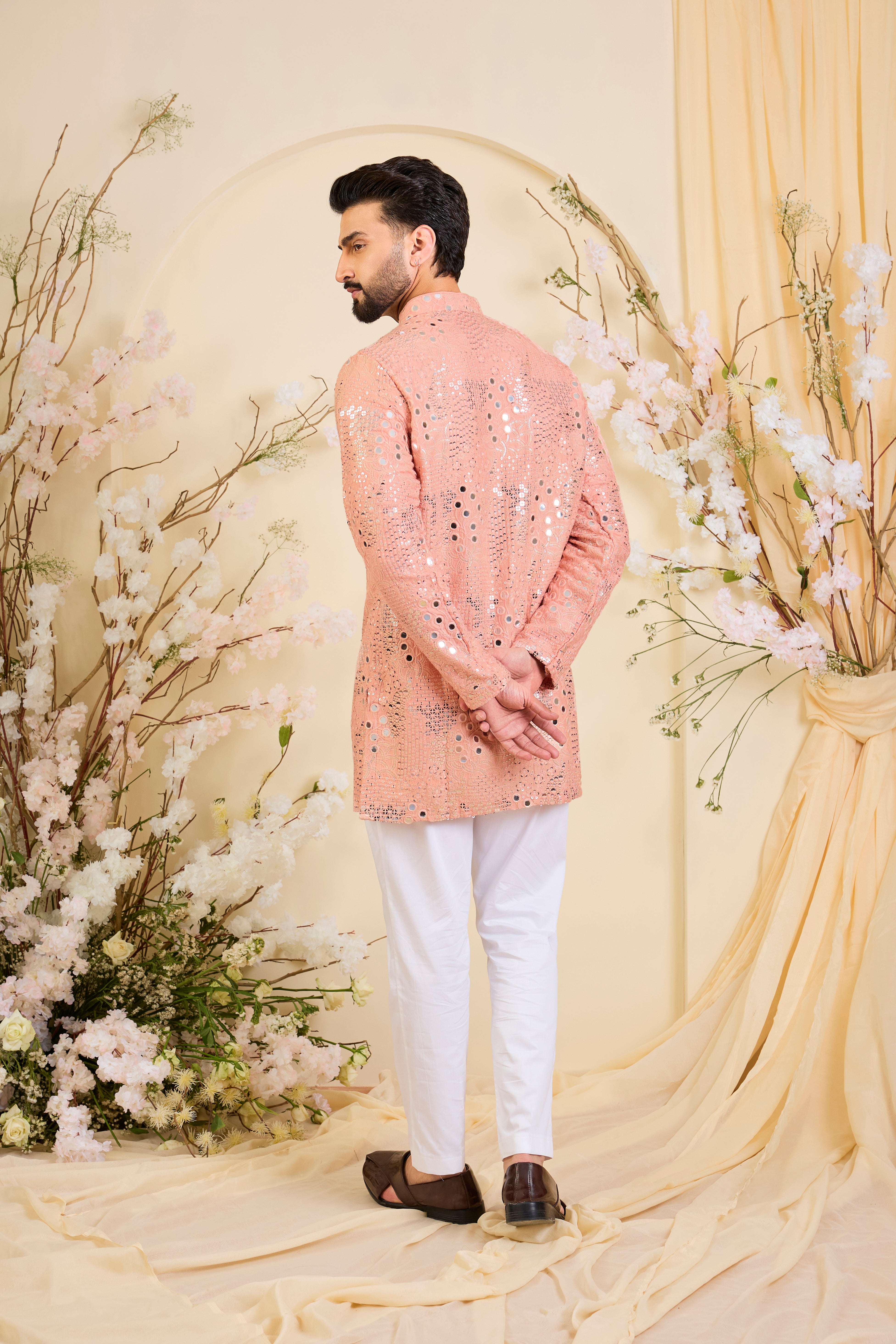 A peach short kurta enriched with intricate mirror work, delicate floral embroidery, and dense sequin detailing.