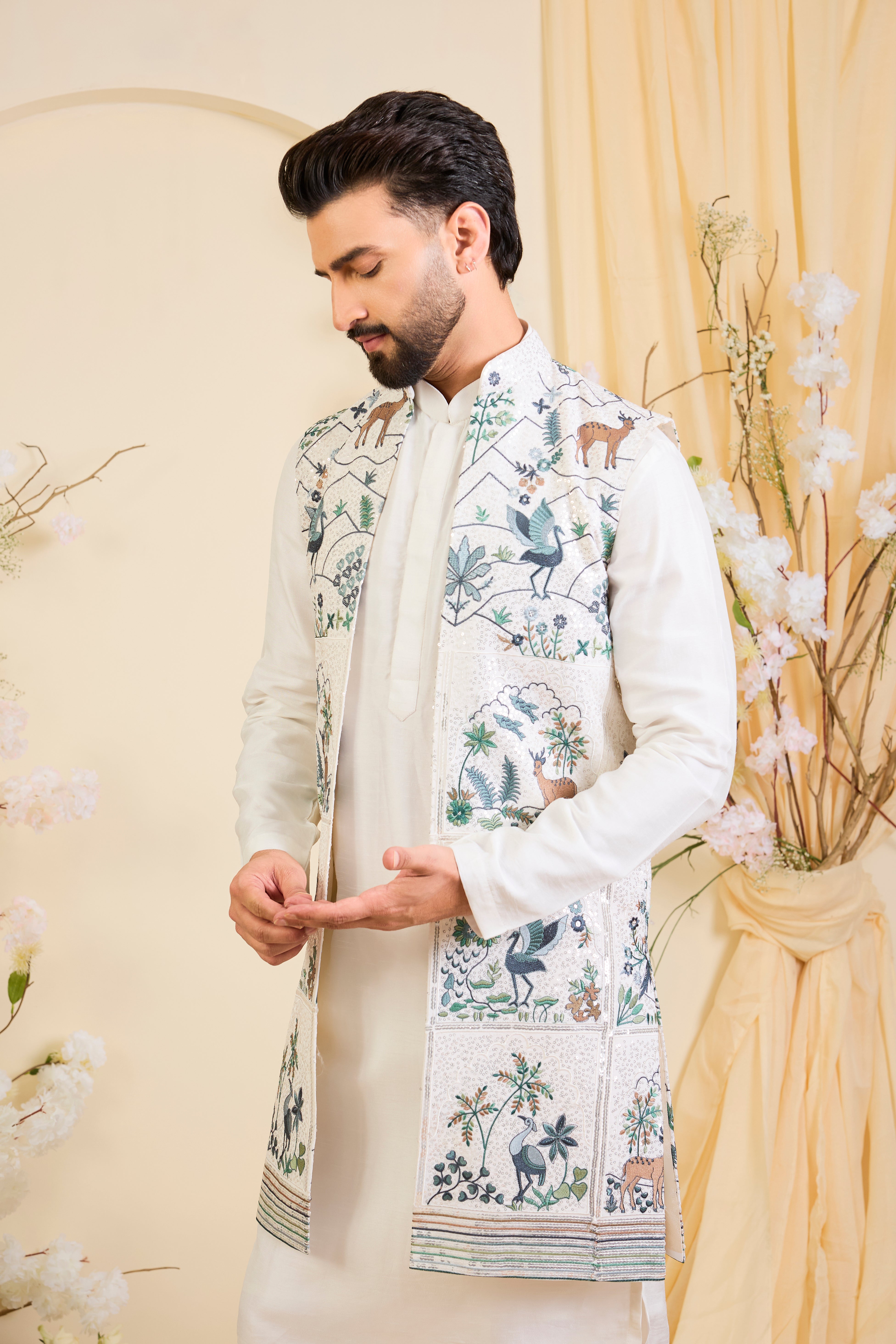 White long open jacket with intricate sequin work and detailed flora-fauna motifs, offering a luminous, richly layered couture statement.