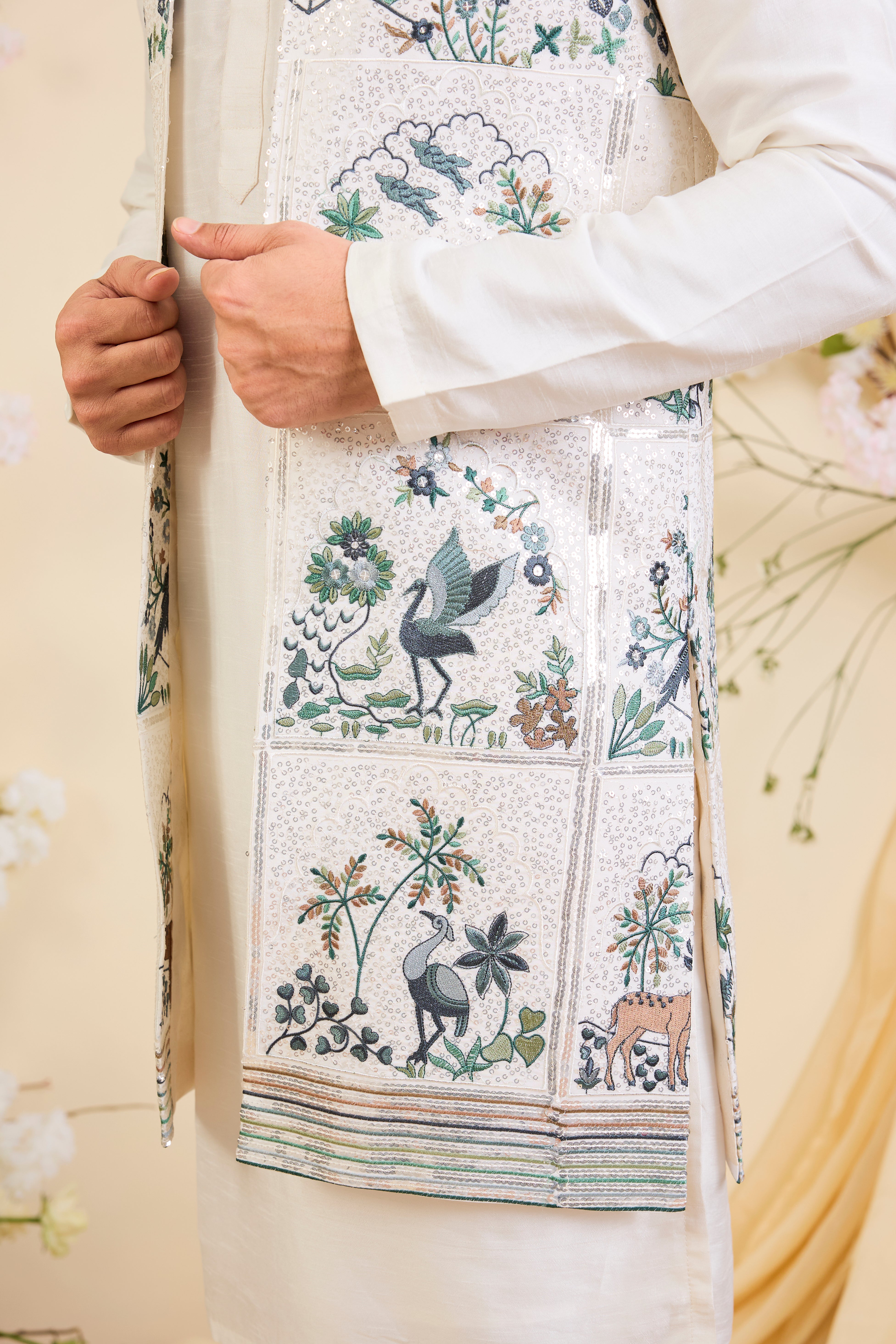 White long open jacket with intricate sequin work and detailed flora-fauna motifs, offering a luminous, richly layered couture statement.