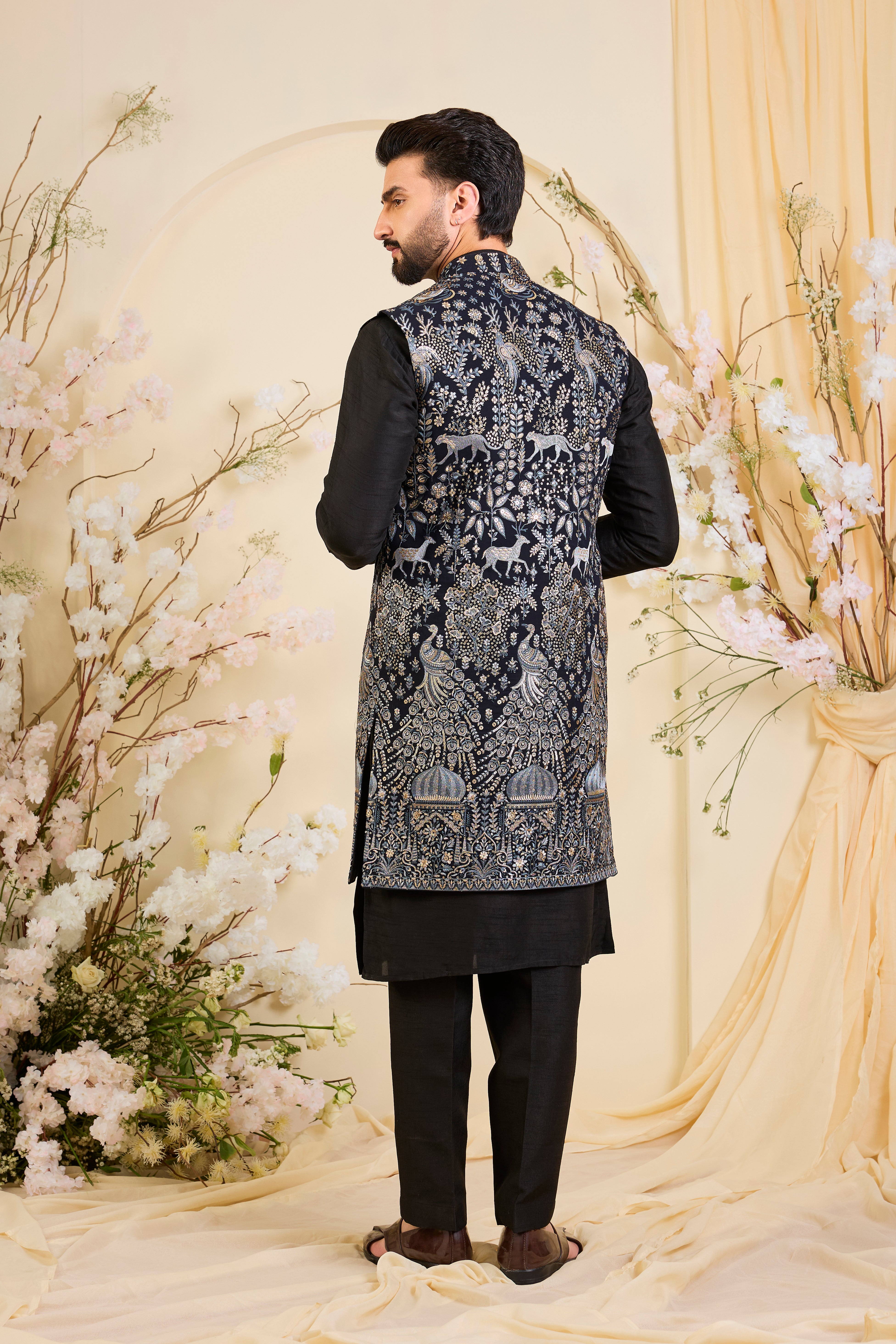 Blue long open jacket with intricate zari work, sequin detailing, and Mughal darbar scenes with flora-fauna motifs, delivering a grand couture statement.