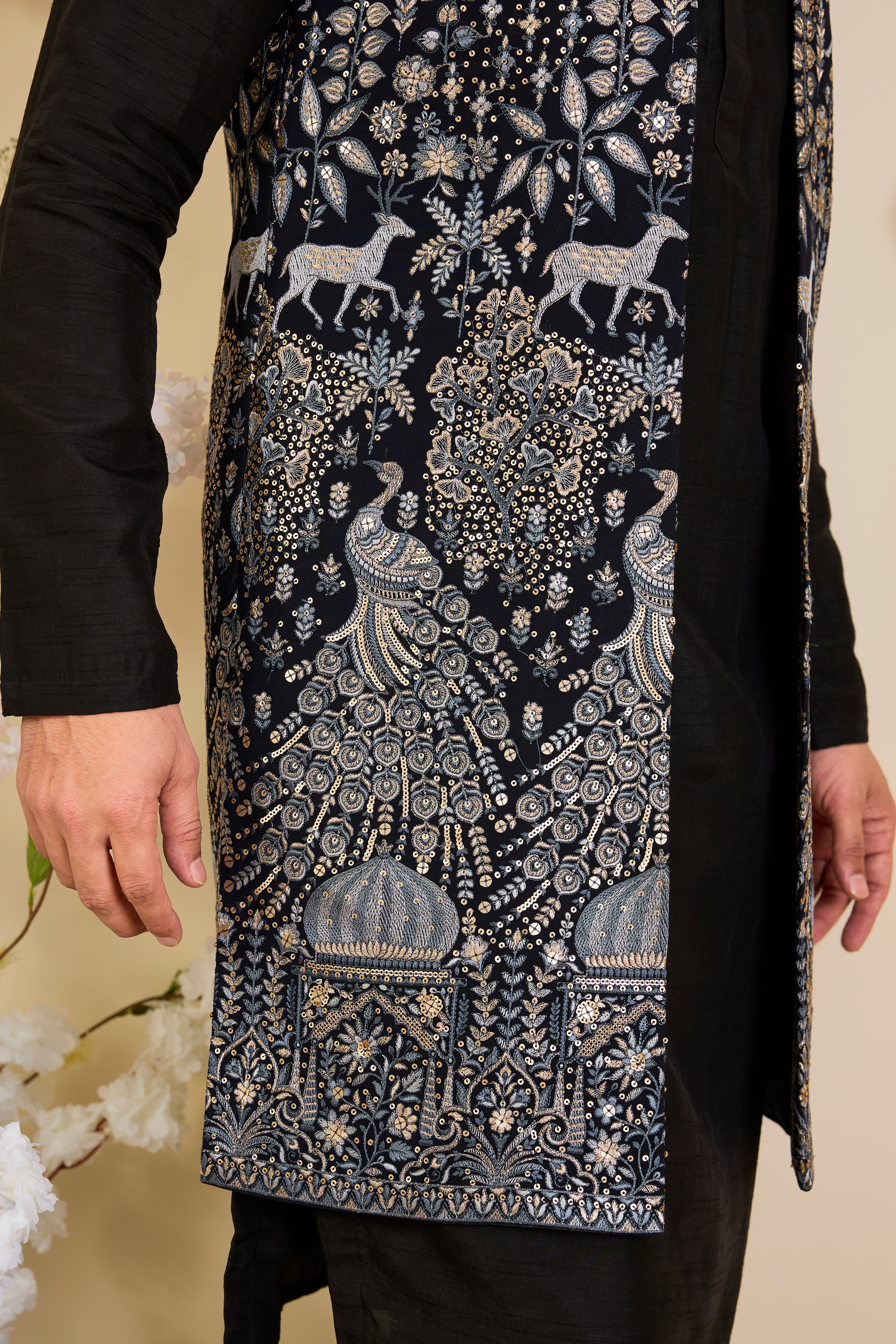 Blue long open jacket with intricate zari work, sequin detailing, and Mughal darbar scenes with flora-fauna motifs, delivering a grand couture statement.