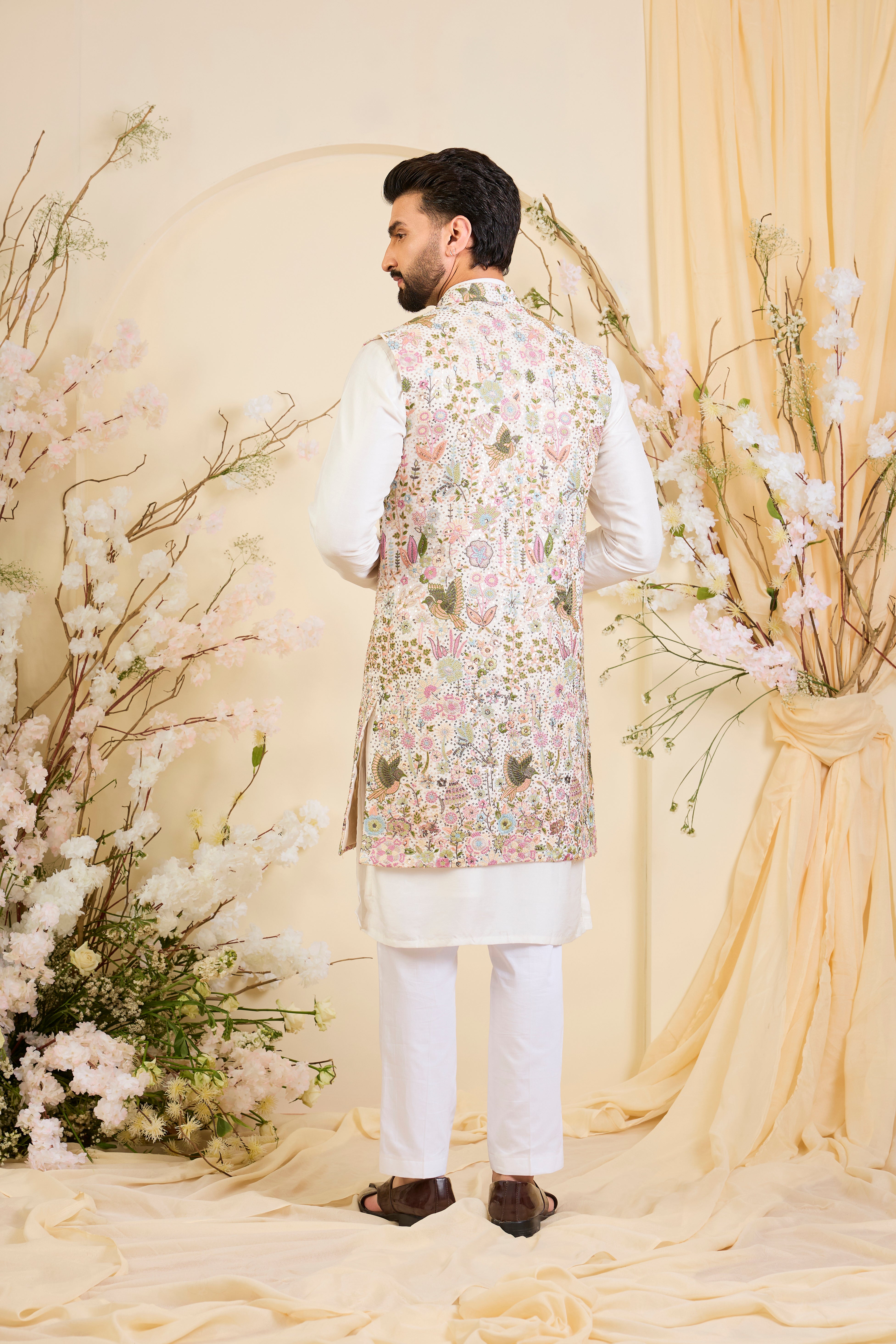 White long open jacket with intricate sequin work and detailed flora-fauna motifs, offering a luminous, richly layered couture statement.