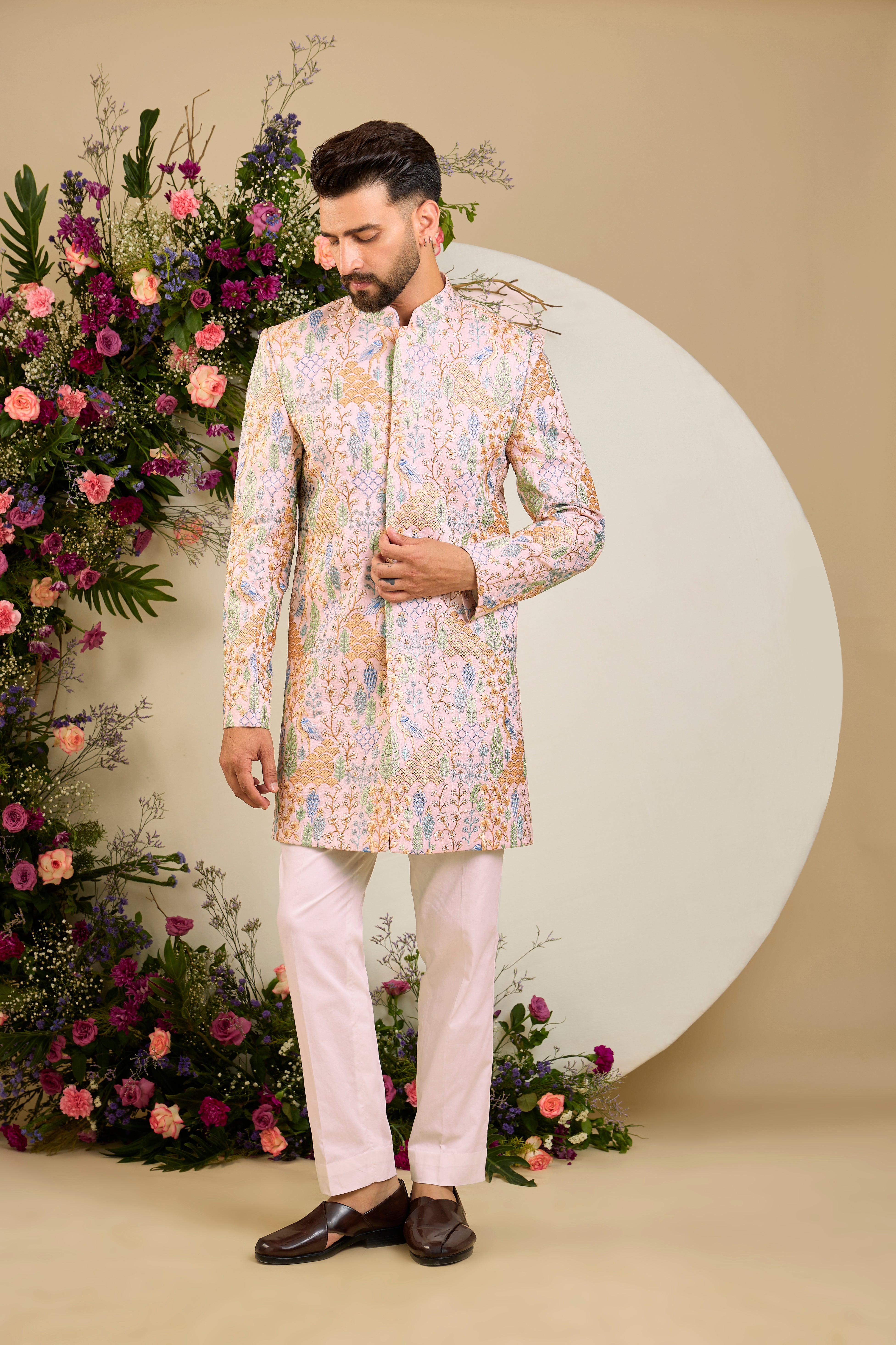 Blush pink short sherwani with tropical flora and fauna embroidery, vibrant threadwork, and delicate sequins for refined formal elegance.