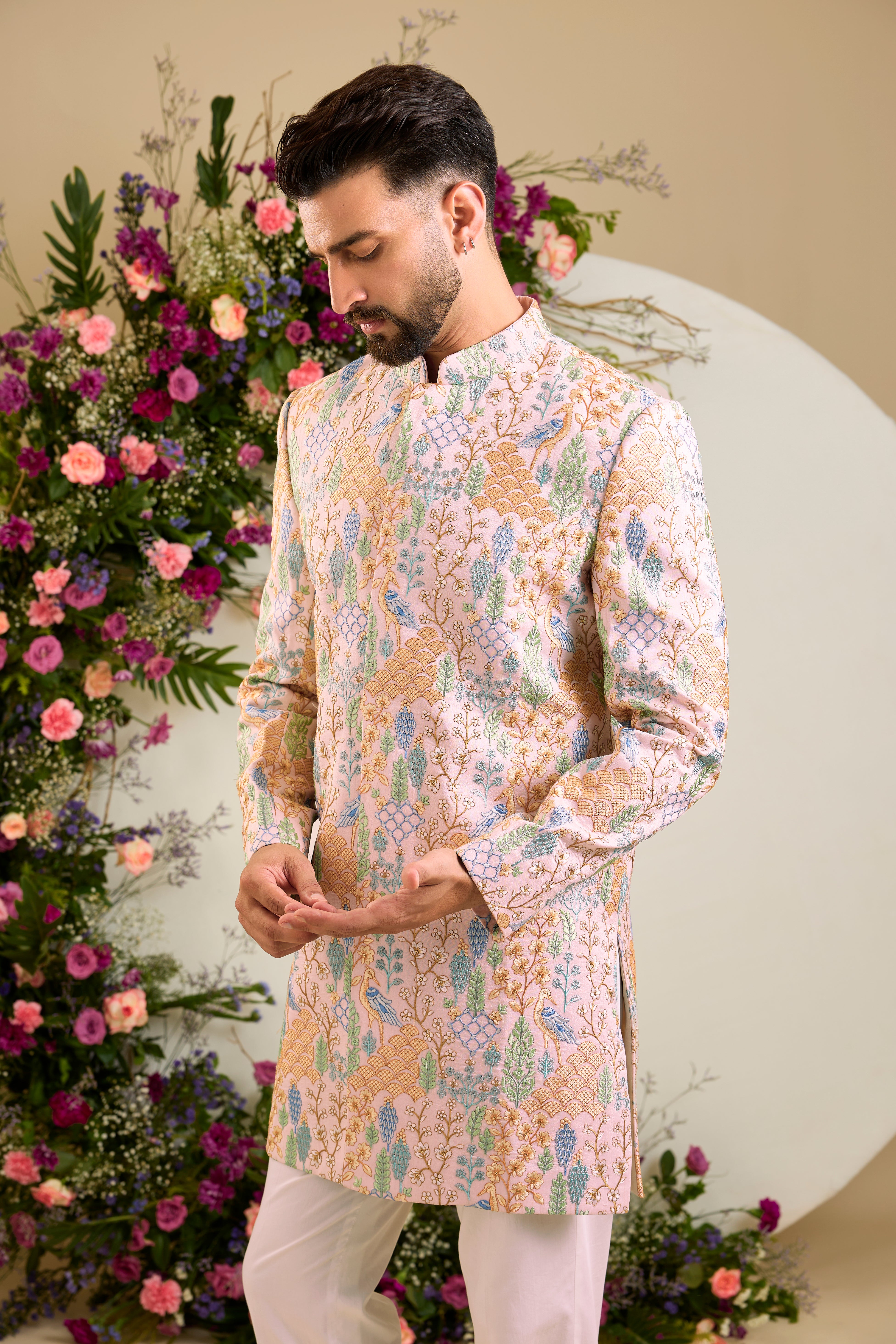 Blush pink short sherwani with tropical flora and fauna embroidery, vibrant threadwork, and delicate sequins for refined formal elegance.