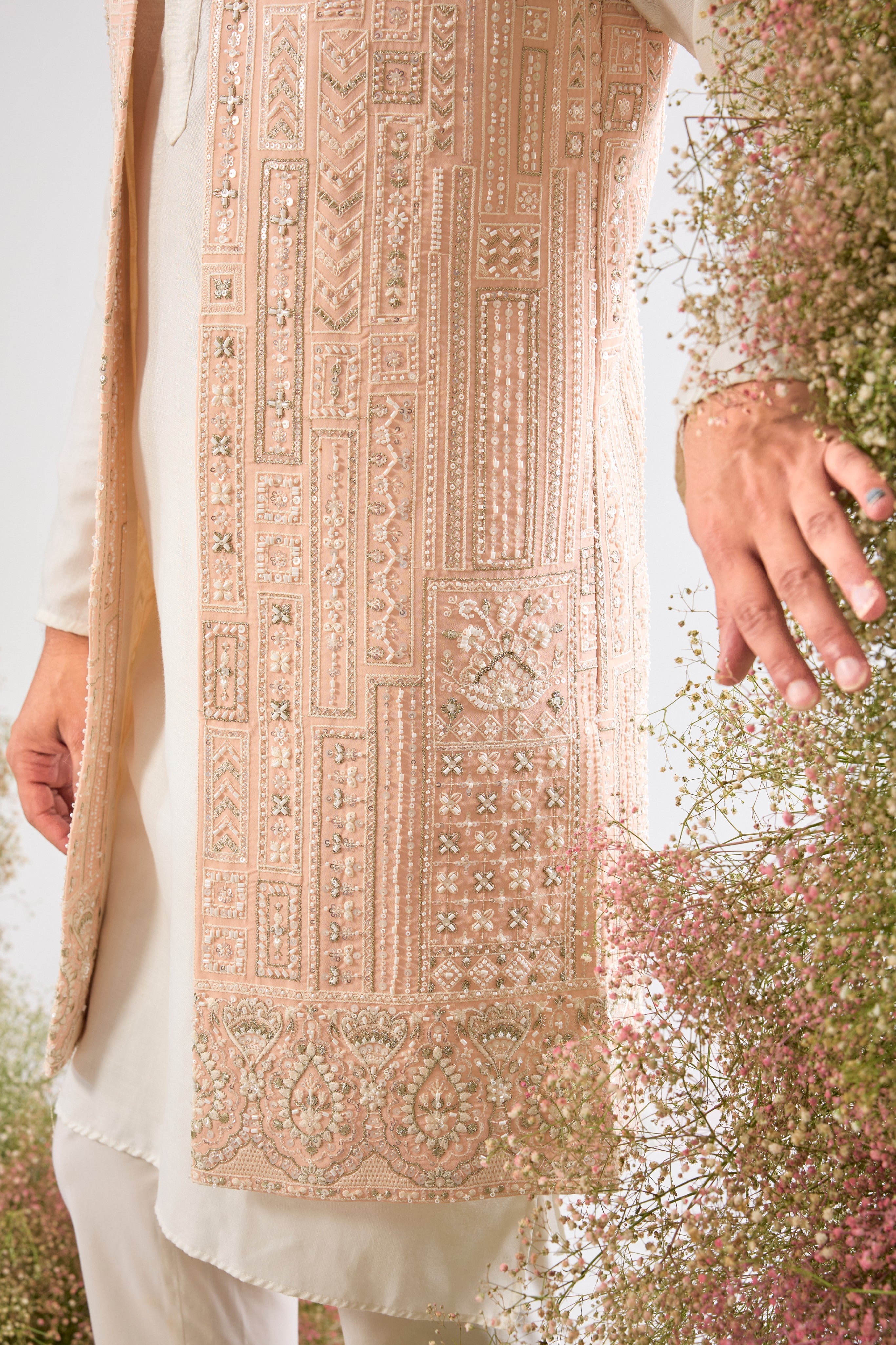 Our Long Open Jacket features exquisite Hind Hand Work, meticulously crafted with shimmering White Cut Dana and Sequin detailing arranged in a sharp Geometrical Pattern. This jacket is the perfect blend of artisanal skill and contemporary design.