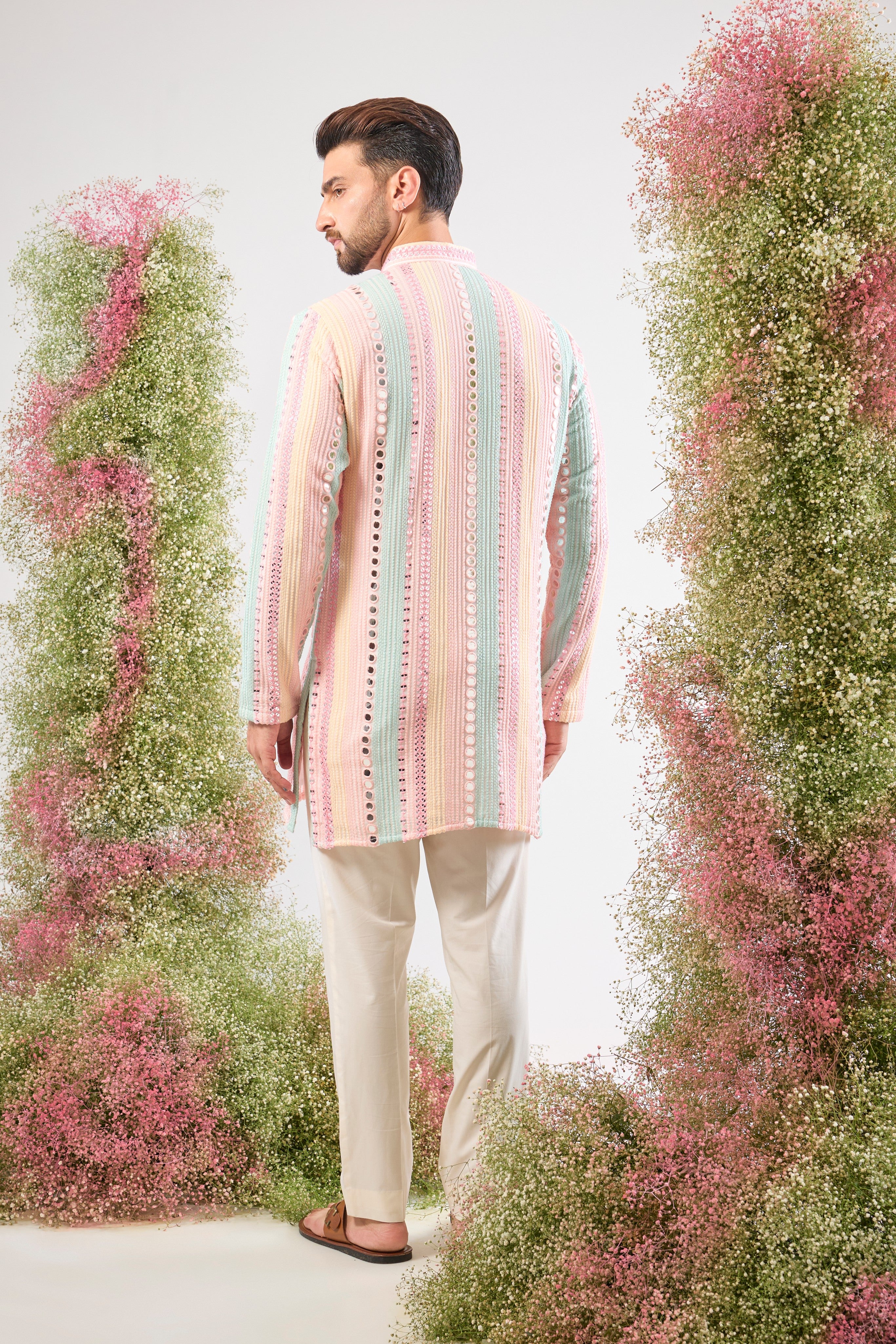 This Short Mirror Work Kurta showcases structured Pintucks Style Stripes filled with rich Multi-coloured Thread work, subtly enhanced by Delicate Sequin Work. The combination is utterly magical, offering a sophisticated yet joyful aesthetic.