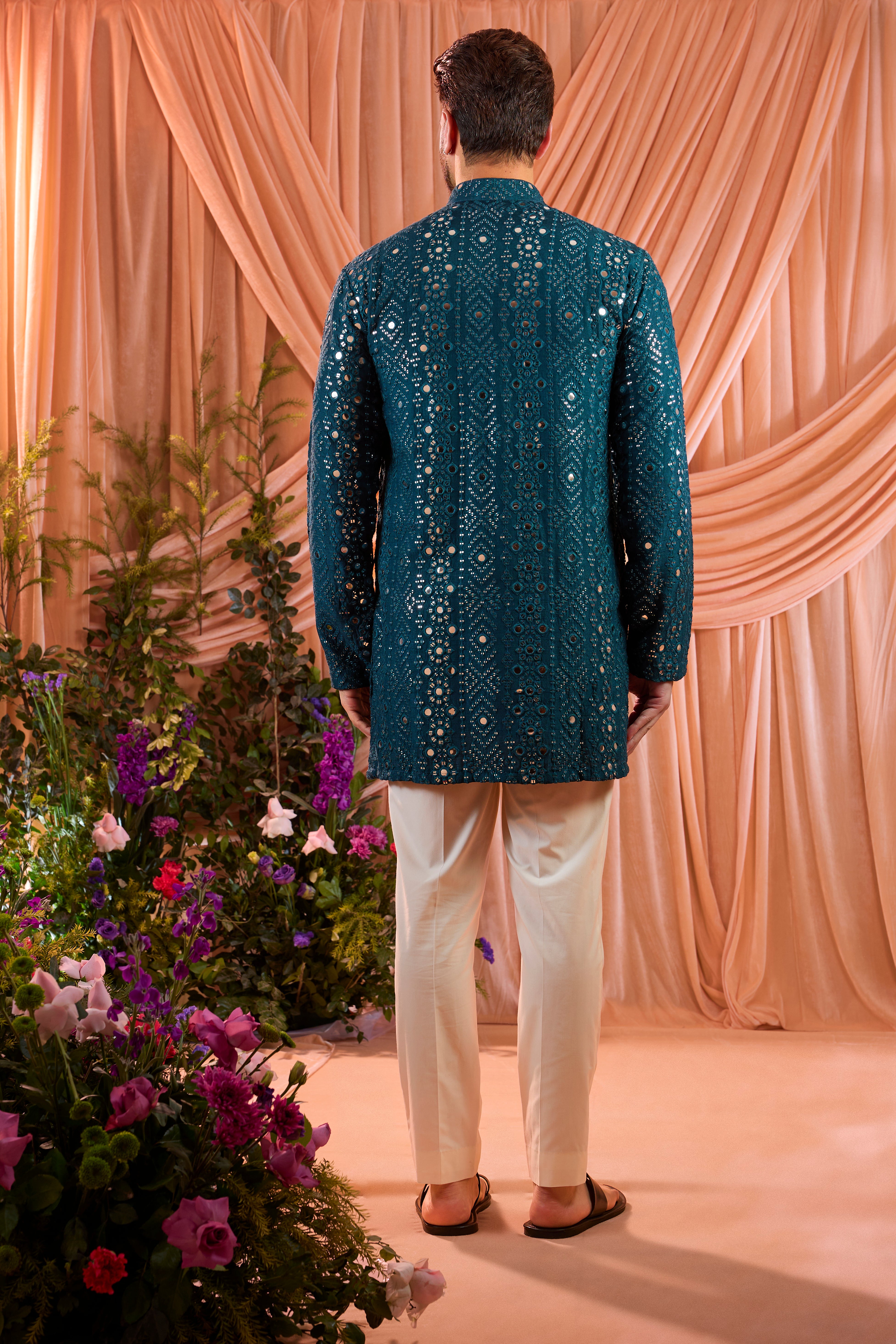 A signature teal short kurta featuring mirror-inspired sequin work that recreates the brilliance of traditional mirror craftsmanship. The refined surface detailing adds depth and controlled shimmer.