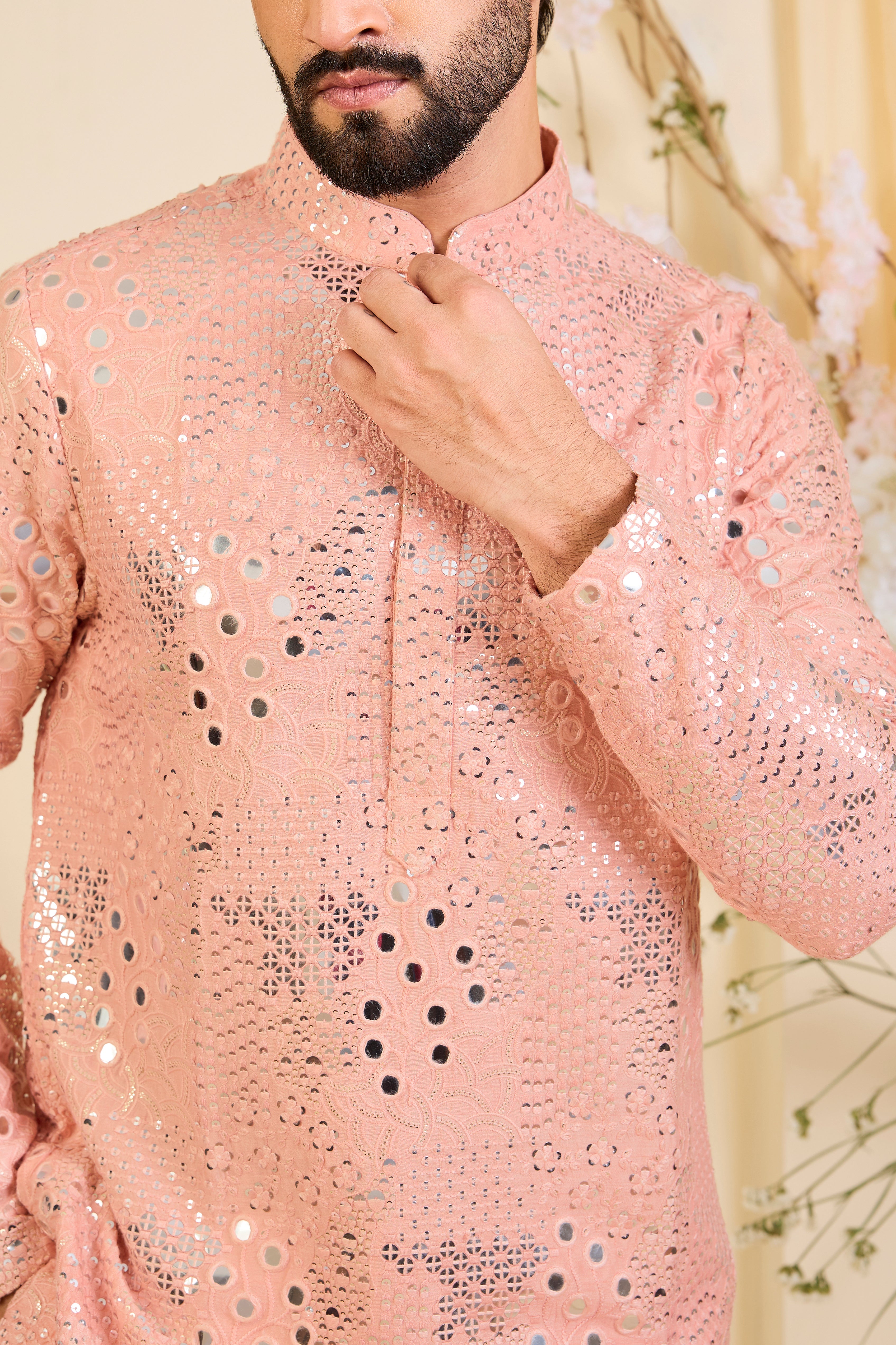 A peach short kurta enriched with intricate mirror work, delicate floral embroidery, and dense sequin detailing.