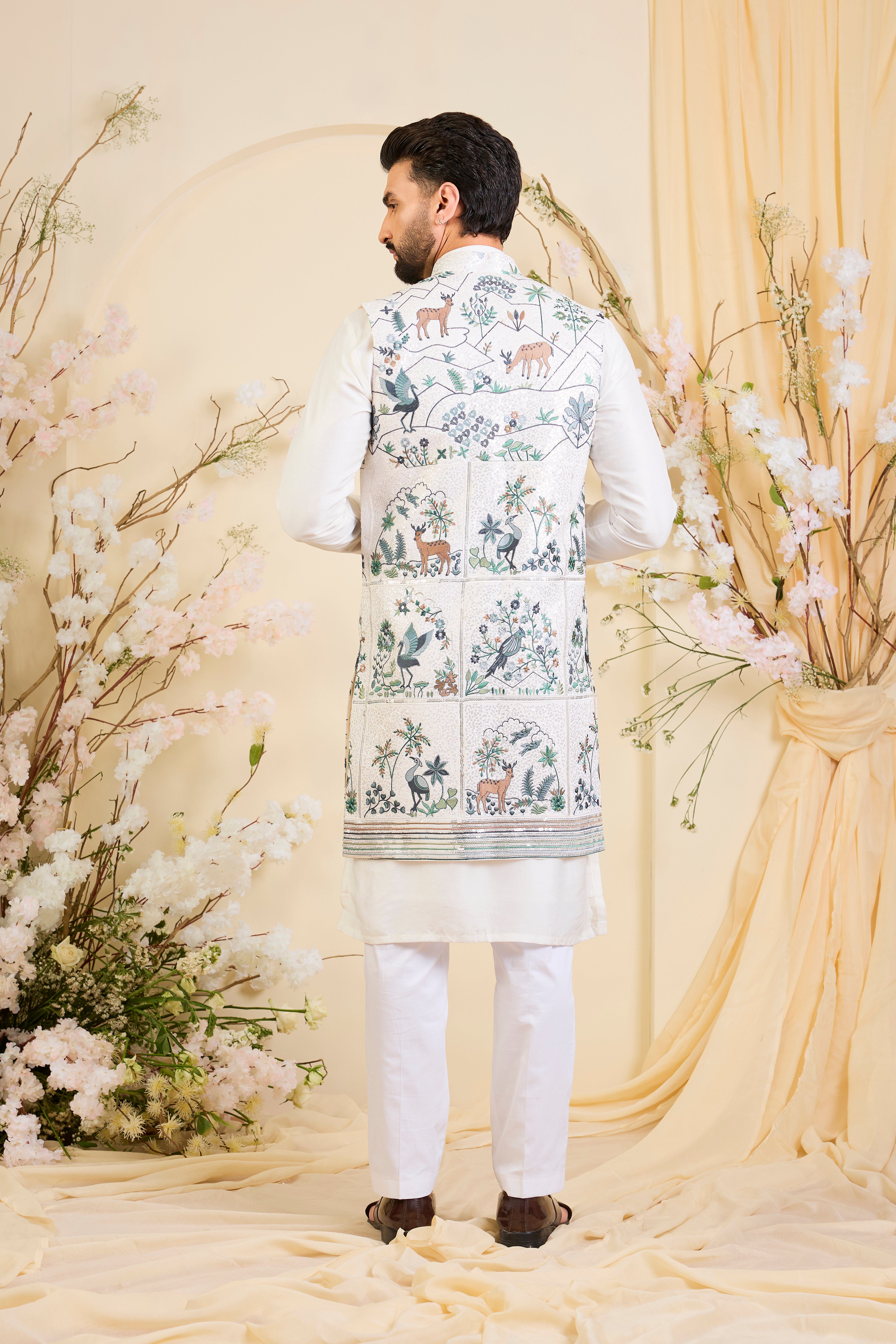White long open jacket with intricate sequin work and detailed flora-fauna motifs, offering a luminous, richly layered couture statement.