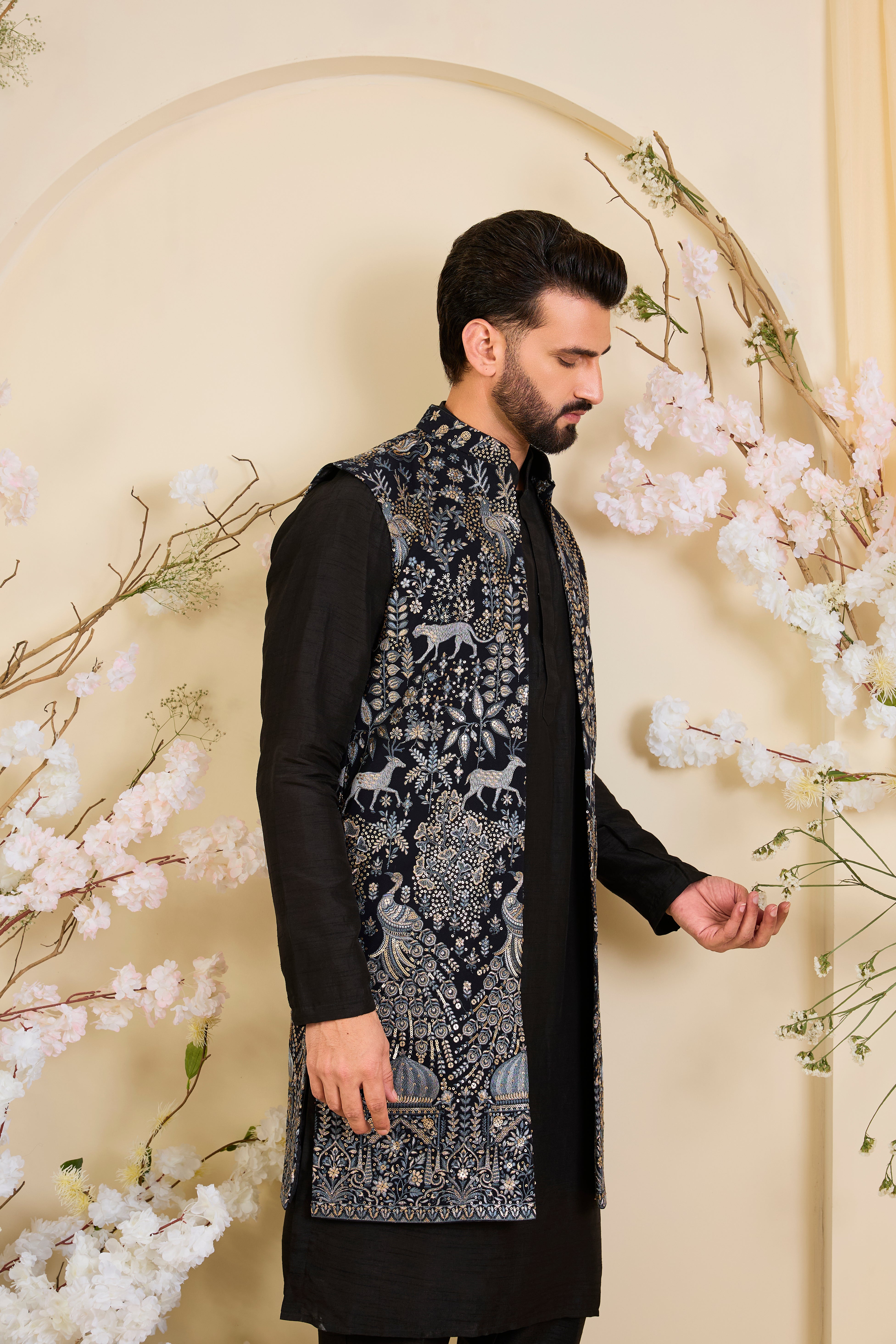 Blue long open jacket with intricate zari work, sequin detailing, and Mughal darbar scenes with flora-fauna motifs, delivering a grand couture statement.
