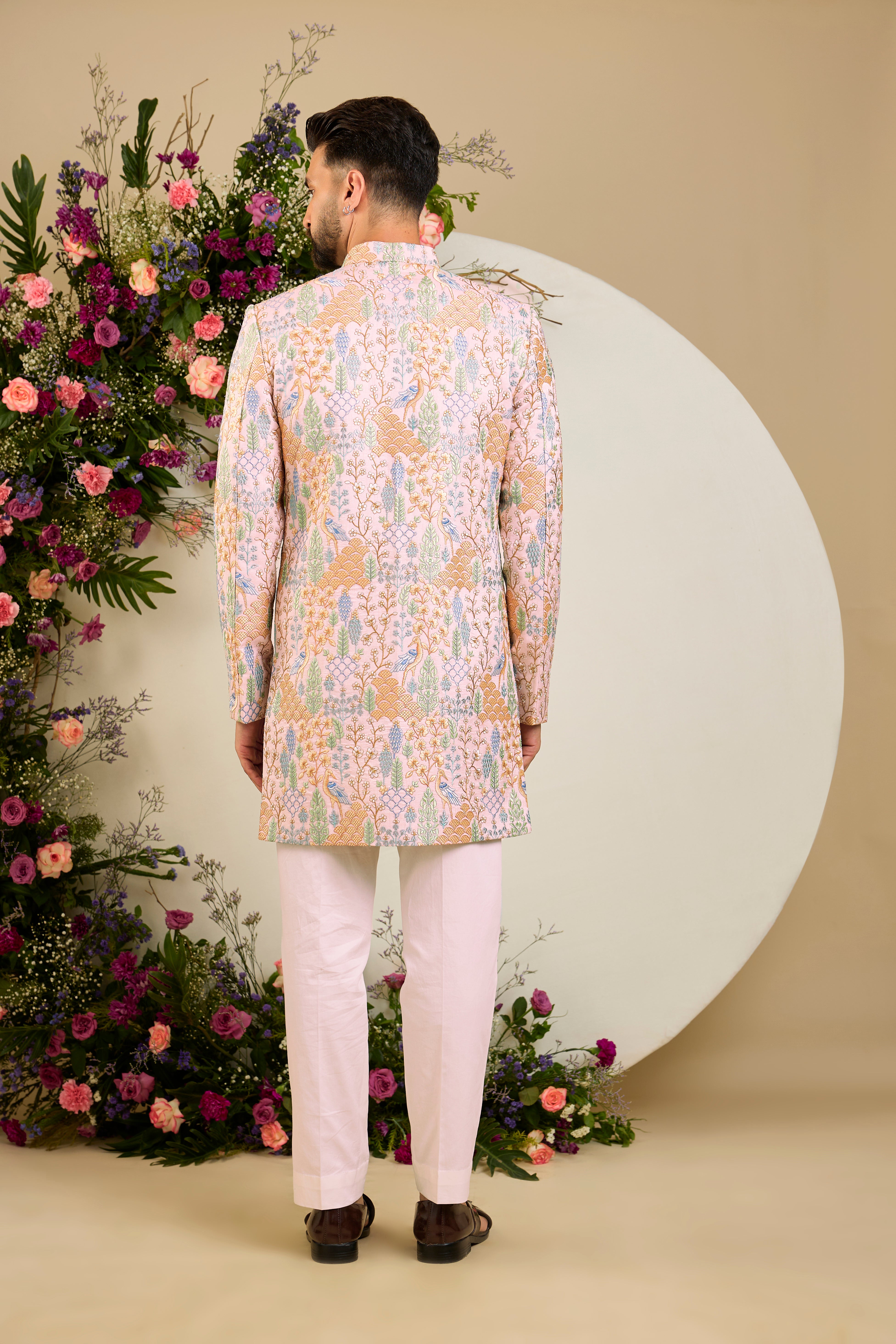 Blush pink short sherwani with tropical flora and fauna embroidery, vibrant threadwork, and delicate sequins for refined formal elegance.