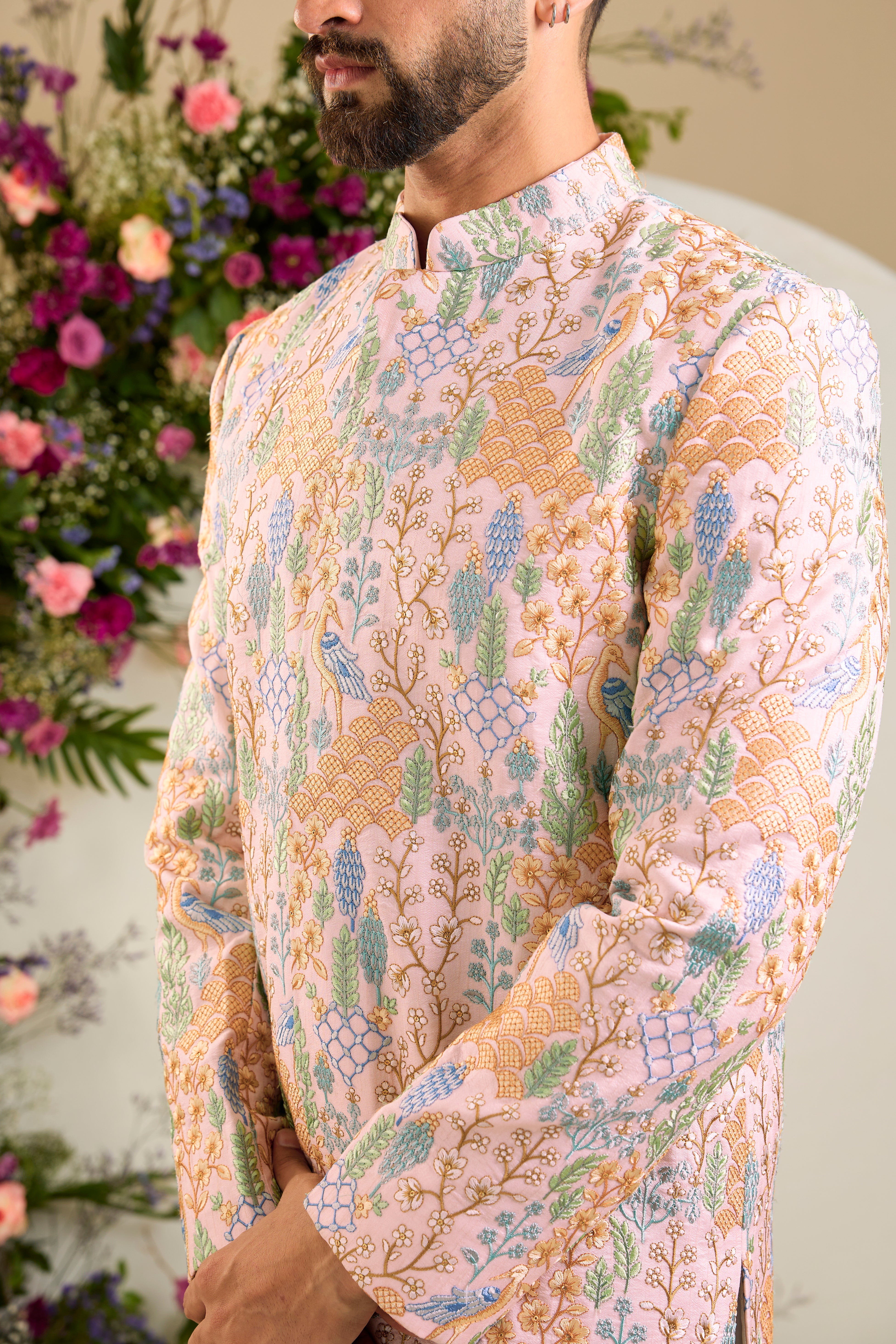Blush pink short sherwani with tropical flora and fauna embroidery, vibrant threadwork, and delicate sequins for refined formal elegance.
