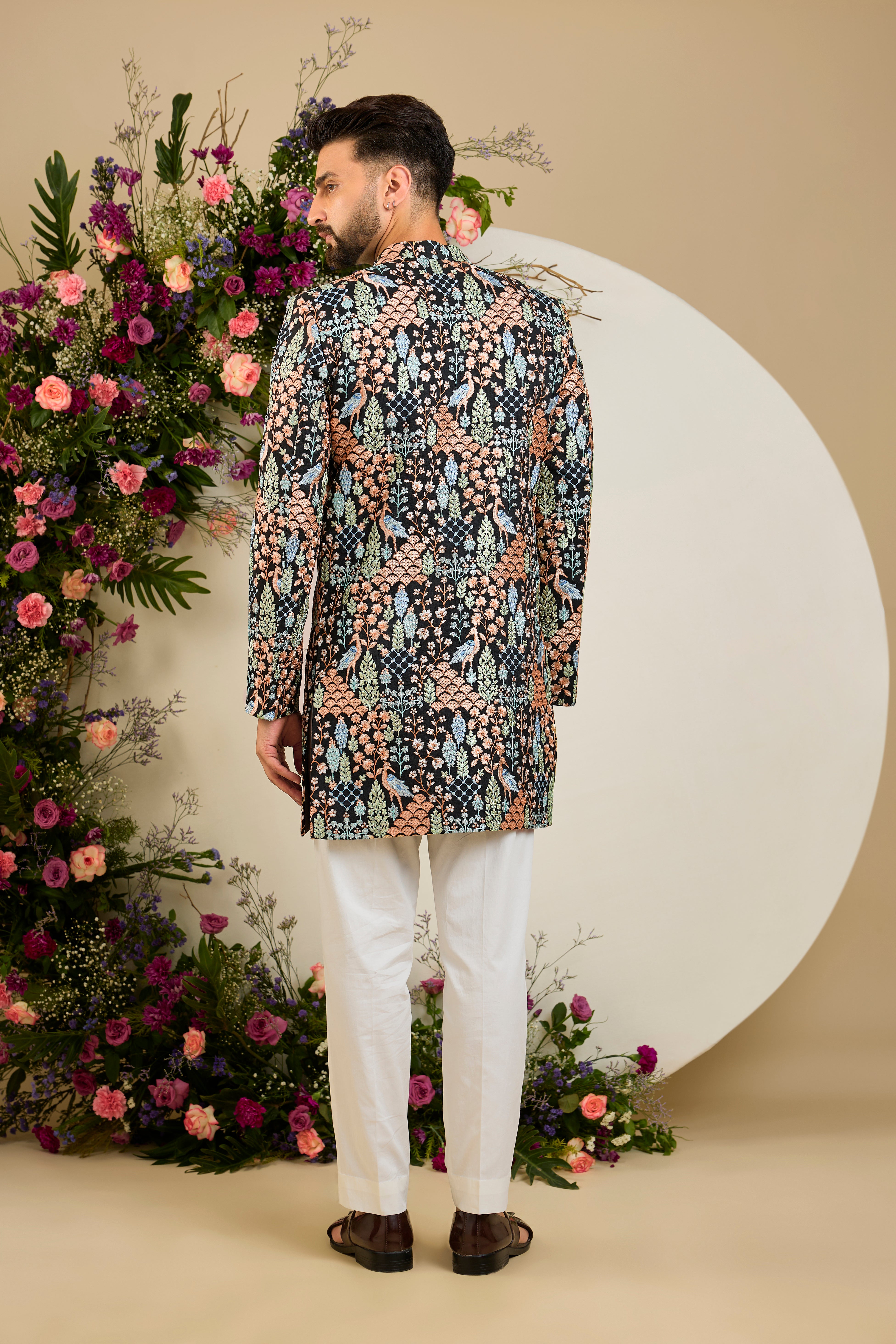 Black short sherwani with tropical flora and fauna embroidery, vibrant threadwork, and delicate sequins for refined formal elegance.