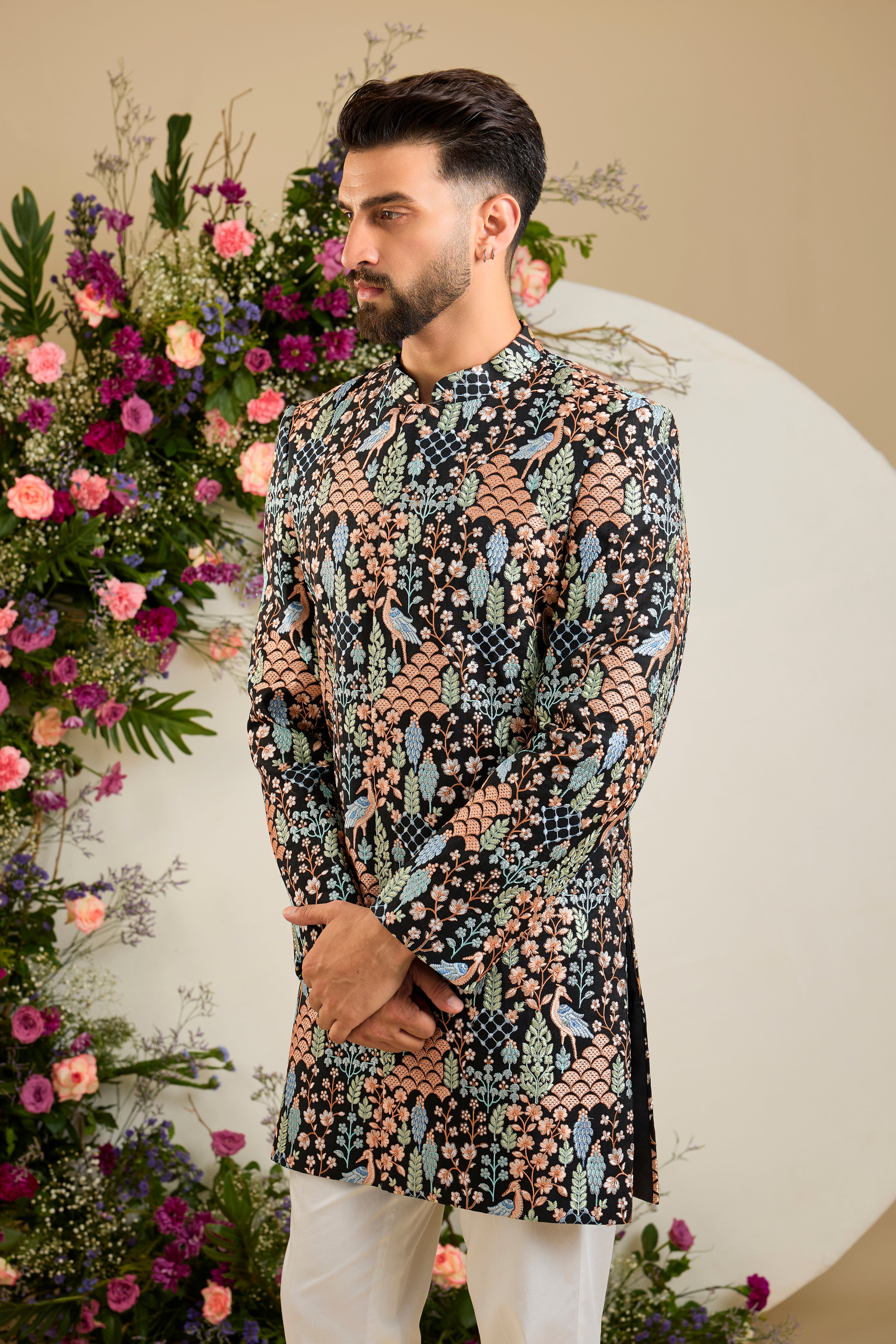 Black short sherwani with tropical flora and fauna embroidery, vibrant threadwork, and delicate sequins for refined formal elegance.