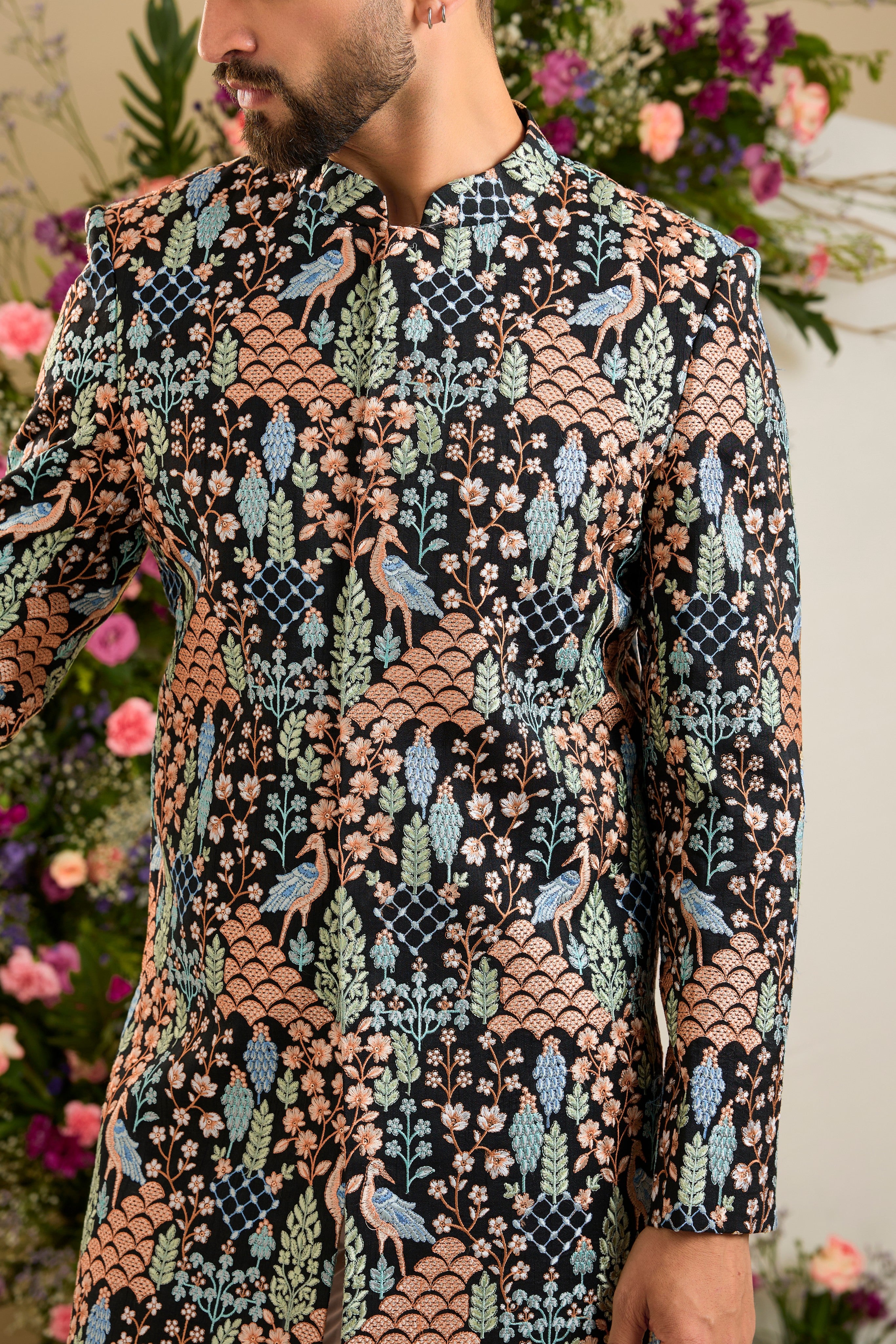 Black short sherwani with tropical flora and fauna embroidery, vibrant threadwork, and delicate sequins for refined formal elegance.