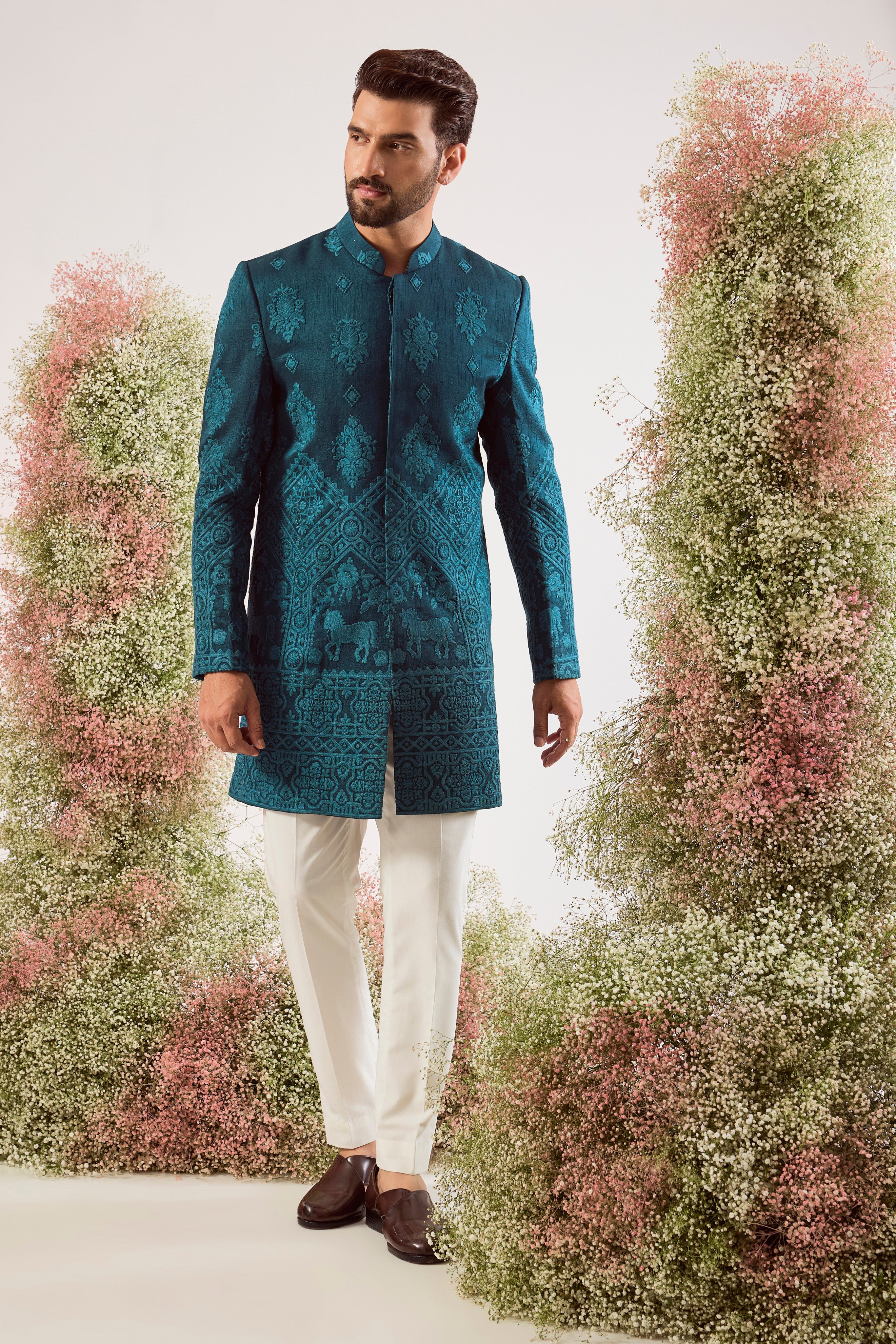This stunning teal thread work short sherwani is a masterpiece of modern artistry. The rich, deep hue provides a luxurious canvas for the intricate threadwork, while the beautifully hand-stitched horse figures add a powerful and distinctive touch.