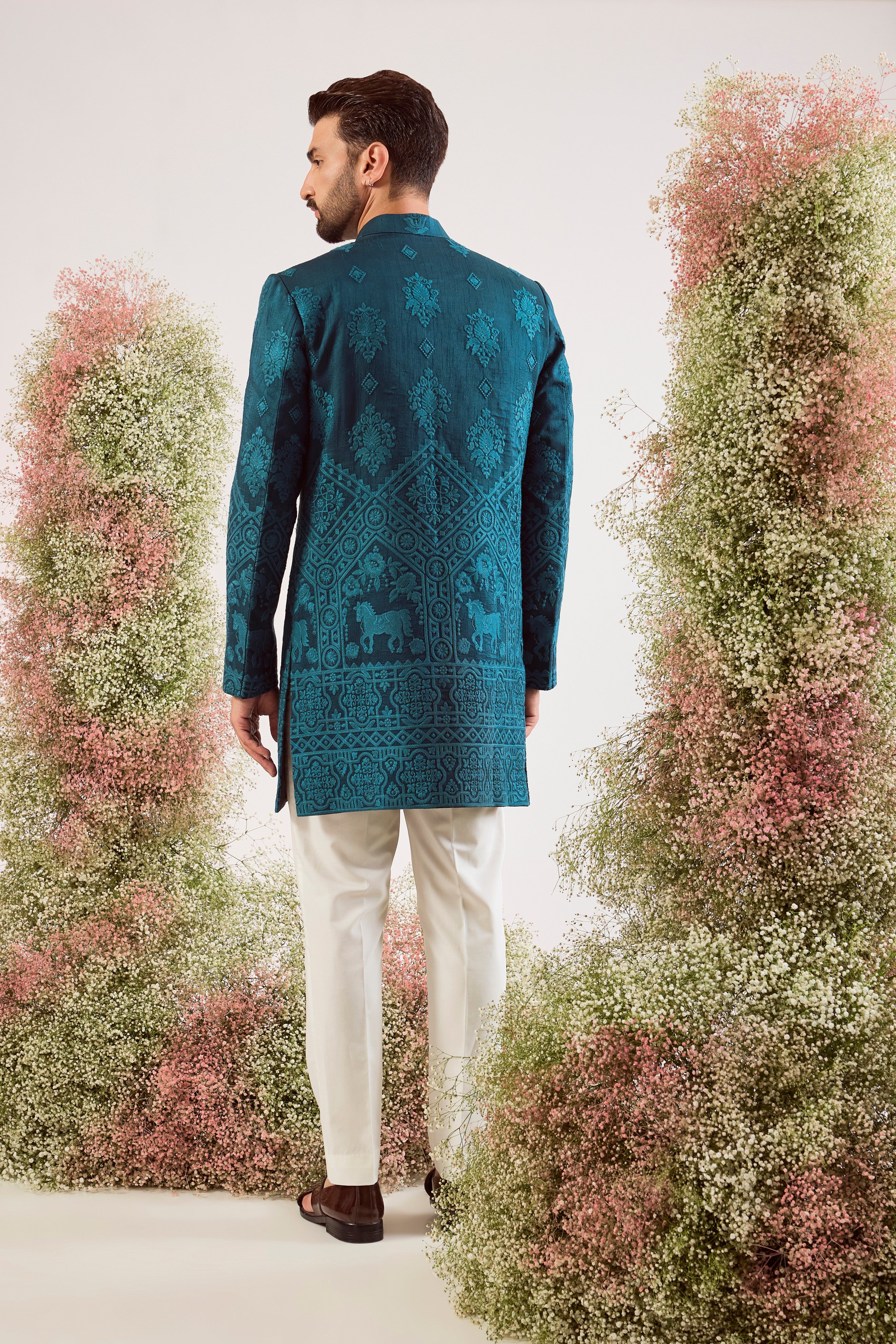 This stunning teal thread work short sherwani is a masterpiece of modern artistry. The rich, deep hue provides a luxurious canvas for the intricate threadwork, while the beautifully hand-stitched horse figures add a powerful and distinctive touch.