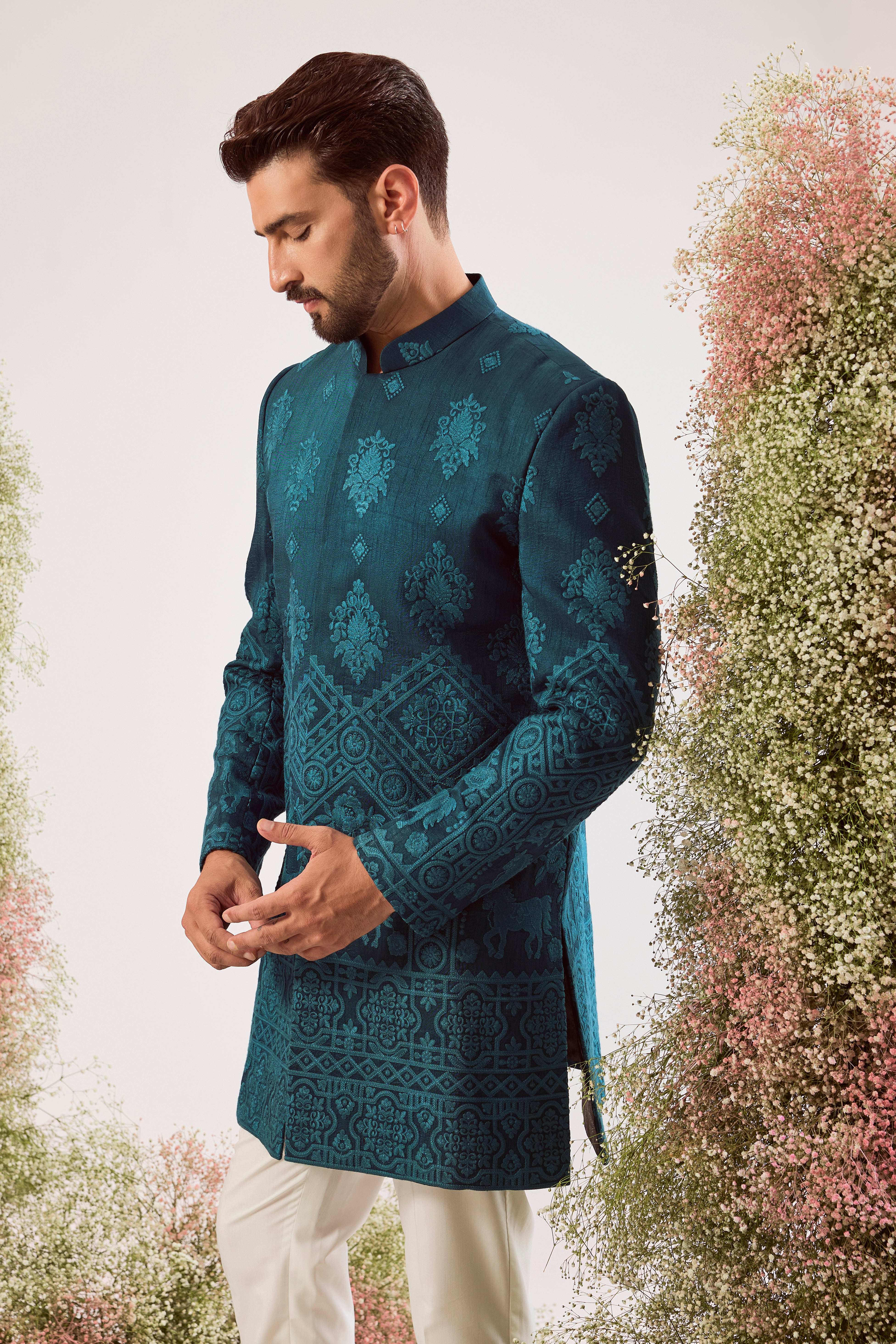 This stunning teal thread work short sherwani is a masterpiece of modern artistry. The rich, deep hue provides a luxurious canvas for the intricate threadwork, while the beautifully hand-stitched horse figures add a powerful and distinctive touch.
