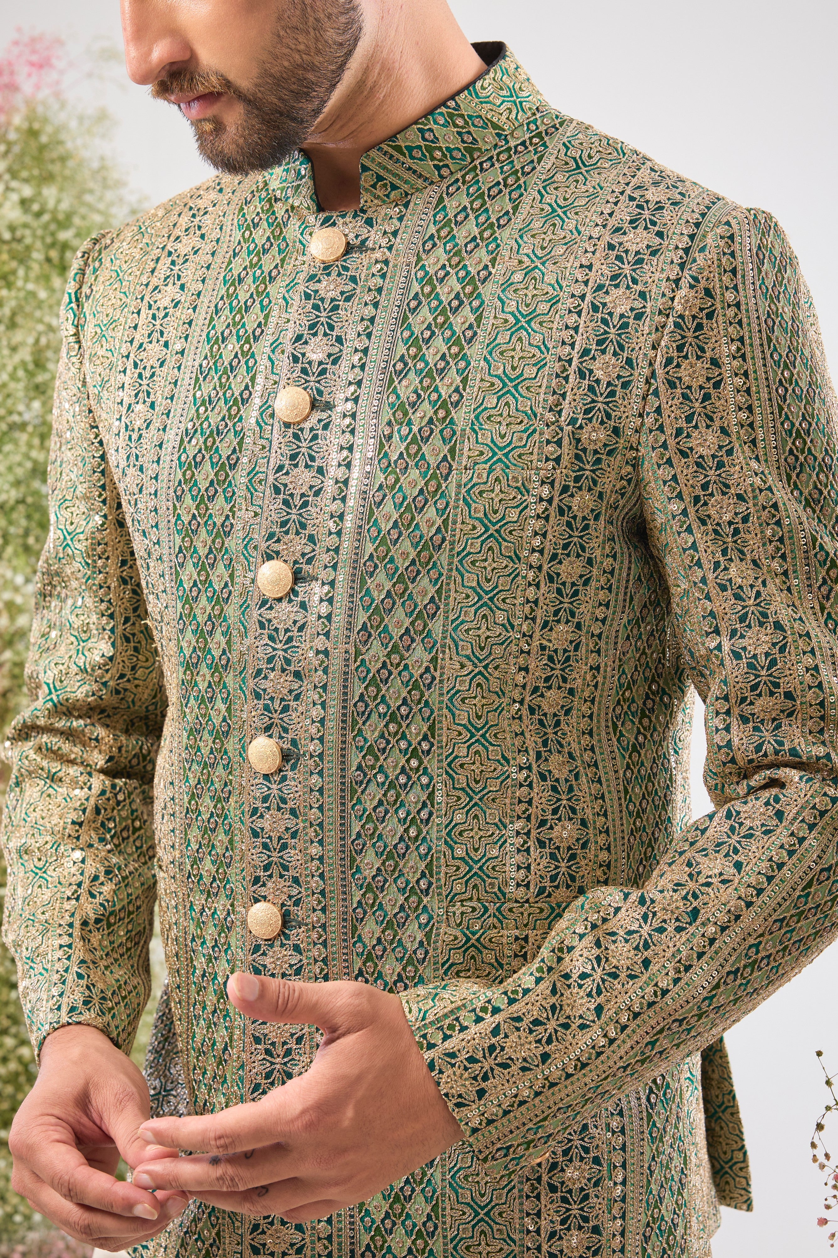 This Bottle Green Bandhgala is lavishly covered in Heavy Zari Work and sequin accents. The inclusion of Classy Metal Buttons ensures every detail of this garment speaks of high sophistication.