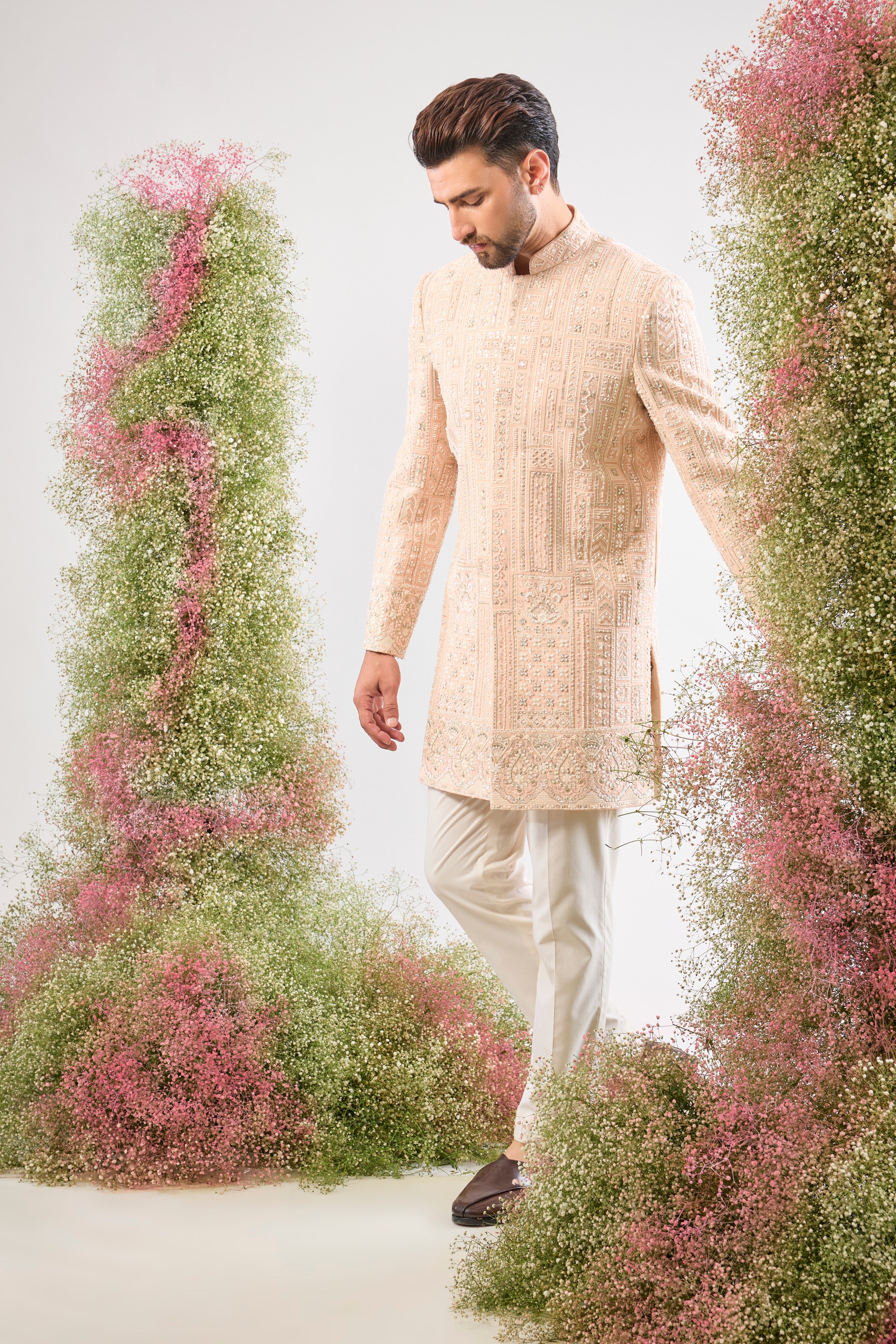 Our Pink Short Sherwani features a striking Geometrically Embroidered pattern, meticulously brought to life with exquisite Hand Work White Cut Dana and Sequin detailing.