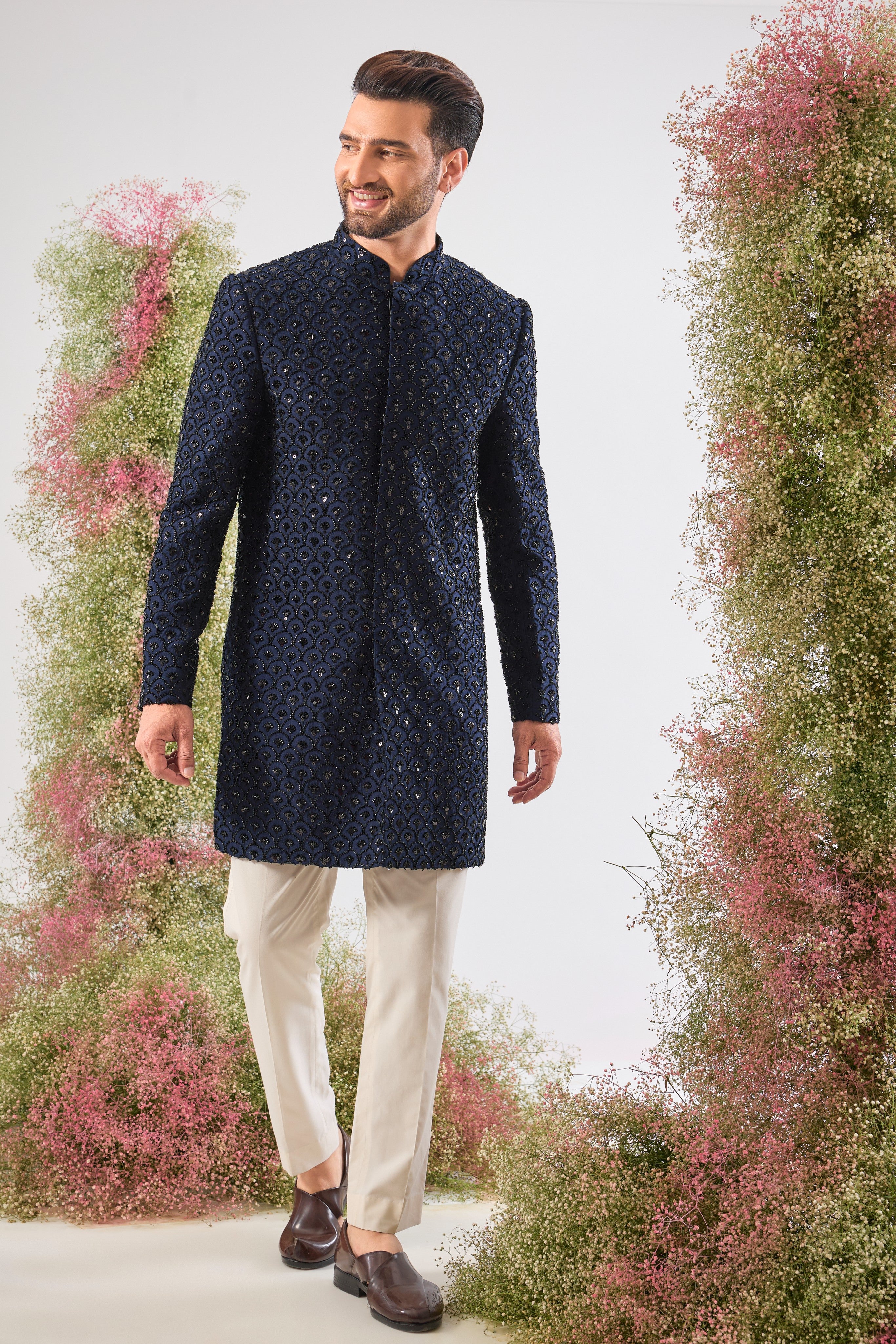 This Short Sherwani showcases a rich, traditional pattern, beautifully contrasted with the subtle, dark sparkle of Hand Embroidered Black Cut Dana.