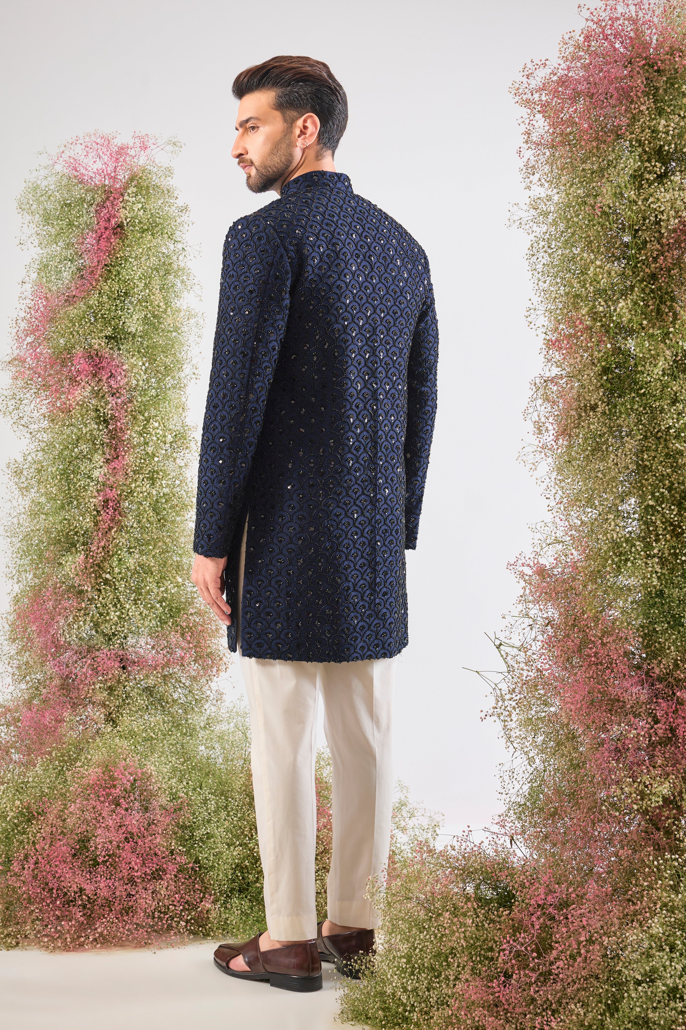 This Short Sherwani showcases a rich, traditional pattern, beautifully contrasted with the subtle, dark sparkle of Hand Embroidered Black Cut Dana.